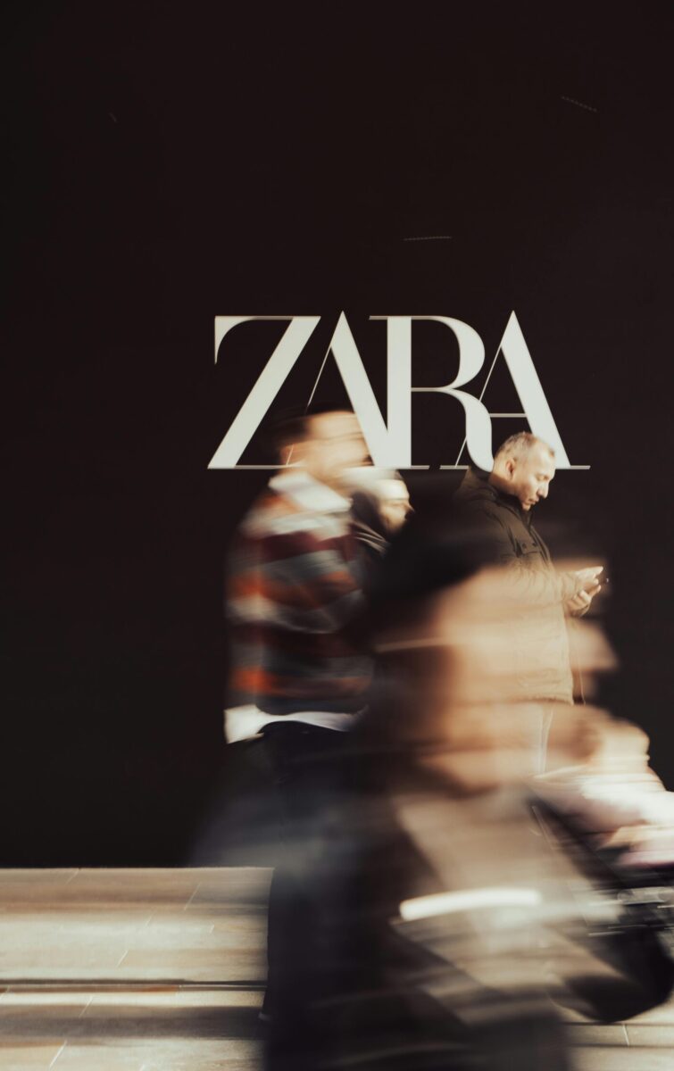 Dynamic blur of people walking past a Zara store facade, capturing urban hustle.